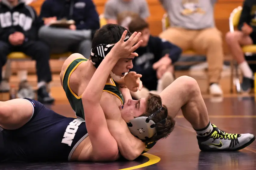 Two men wrestling on a mat in front of other people.